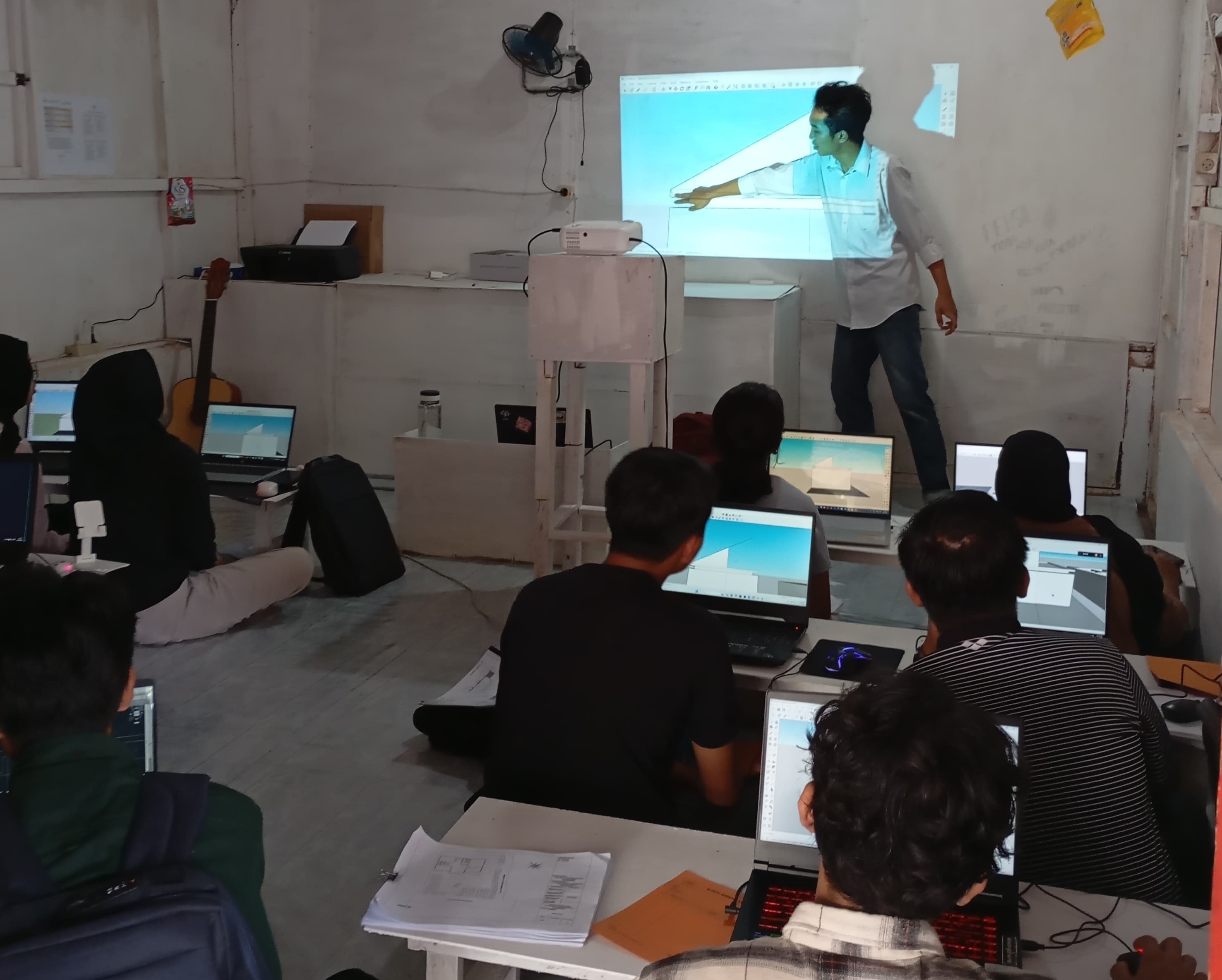 Sesi pembelajaran komunitas dengan mentor sedang menjelaskan konsep desain 3D di papan tulis 